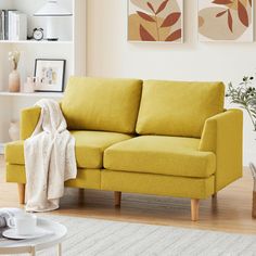 a living room with a yellow couch and two pictures on the wall above it,