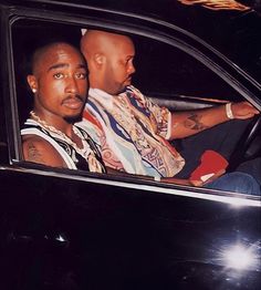 two men sitting in the driver's seat of a car, one with his arm around the other