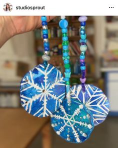 two snowflakes are hanging from a beaded necklace on a table in front of a bookshelf