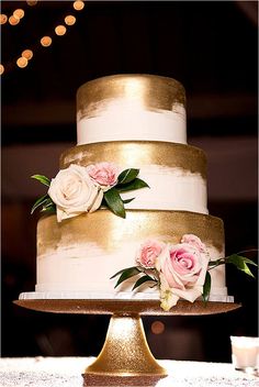 a wedding cake with gold and white frosting decorated with pink roses on the side