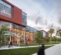 two people walking on the sidewalk in front of a building with glass walls and trees