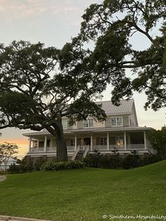 a large white house sitting on top of a lush green field next to a tree