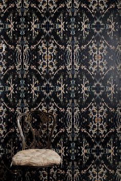 a chair sitting in front of a black wall with an intricate design on it's back