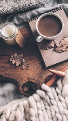 a cup of coffee on top of a wooden table next to a knitted blanket