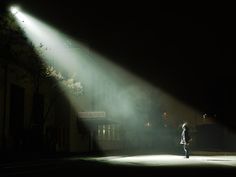 a person standing in the middle of a dark street at night with light shining on them