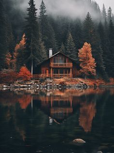 a cabin sits on the shore of a lake surrounded by pine trees and foggy mountains