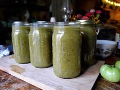 four jars filled with green smoothie sitting on top of a wooden cutting board next to an apple