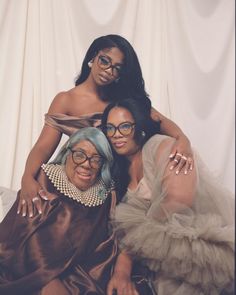 two women pose for the camera in front of a white backdrop, one wearing glasses and the other with blue hair