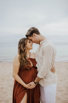 a man and woman standing next to each other on top of a sandy beach with the ocean in the background