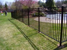 a black metal fence in the middle of a grassy area with people walking around it