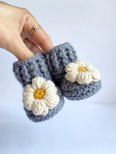 a hand is holding up two crocheted slippers with white and yellow flowers