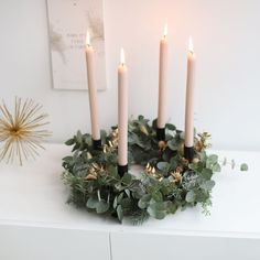 four candles are lit on top of a wreath with greenery and gold stars in the background