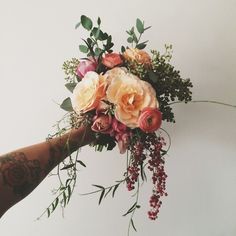 a person's arm holding a bouquet of flowers and greenery in front of a white wall