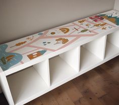 a white bench with colorful designs on the top and bottom shelf next to a wooden floor