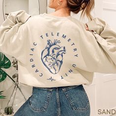 This Cardiac Telemetry Unit Sweatshirt / Telemetry Nurse Sweater is perfect for work! Cozy and warm, it makes a great gift too!   **FRONT & BACK PRINT**  **UNISEX SIZING** ♥ W E L C O M E  T O  S K E T C H Y  C A T  D E S I G N S ! ♥ Click here to return to our shop's home page ⇒ https://www.etsy.com/shop/SketchyCatDesigns Say hello to your new favorite sweatshirt! All products are printed with eco-friendly water-based inks, giving them the softest feel. The design itself is embedded into the fa Cute Healthcare Shirts, Med Surg Nurse Shirt, Nurse Sweatshirt Ideas, Nursing Art, Cardiac Shirt, Telemetry Nursing, Nursing Crewneck, Cardiac Nurse Sweatshirt, Vascular Access Nurse Shirt