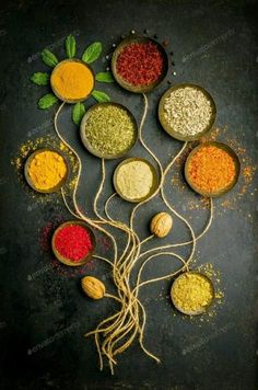 various spices are arranged in bowls on a black surface with green leaves and other ingredients