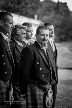 a group of men in kilts standing next to each other on a grass covered field