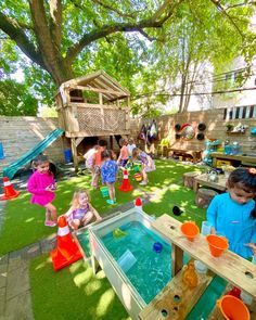 children playing in an outdoor play area with water and sand toys on the grass, surrounded by trees