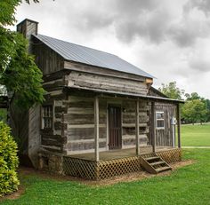 an old log cabin sits in the middle of a grassy field with stairs leading up to it