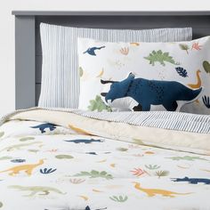 a bed with dinosaurs on the sheets and pillow cases in blue, green, yellow and white