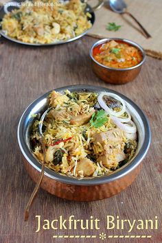 two silver bowls filled with food on top of a wooden table next to spoons