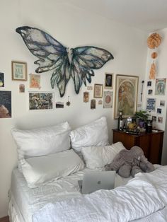 a laptop computer sitting on top of a bed covered in white sheets and pillows with butterfly artwork above it