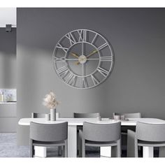 a large clock mounted to the side of a wall above a dining room table with chairs