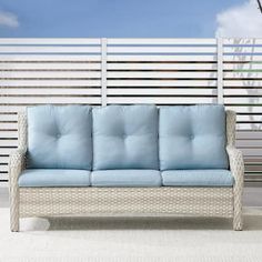 a blue couch sitting on top of a white floor next to a wooden fence and palm tree