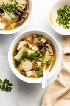 two white bowls filled with soup on top of a marble counter topped with green onions