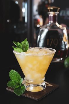 a glass filled with lemonade and mint on top of a wooden table next to a bottle