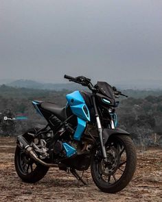 a blue and black motorcycle parked on top of a dirt field next to trees in the distance