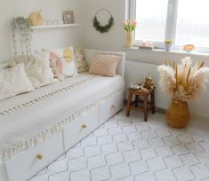 a white daybed with pillows and blankets in a room next to a small table