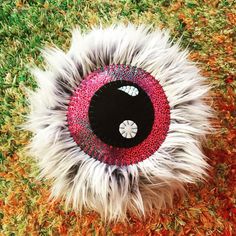 a white and black animal eyeball laying on top of green grass covered in red and orange flecks