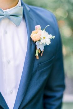 a man in a blue suit and bow tie wearing a boutonniere with flowers on the lapel