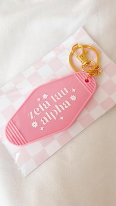 a pink bottle shaped keychain sitting on top of a piece of paper that says zeta ya alpaba