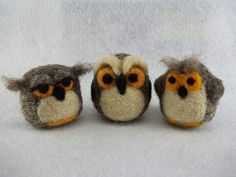 three small stuffed owls sitting next to each other on a white surface with orange eyes