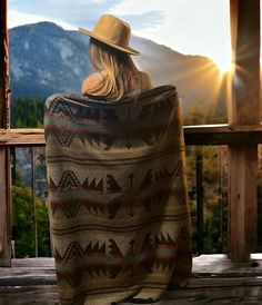 a woman sitting on a porch with a blanket over her head and mountains in the background