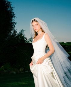 a woman in a white wedding dress posing for the camera with her veil over her head