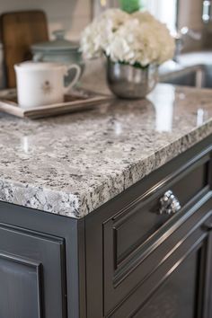 a kitchen island with marble counter tops and gray cabinets in the center, surrounded by white flowers