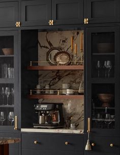 a kitchen with black cabinets and marble counter tops, gold pulls on the doors to open shelves