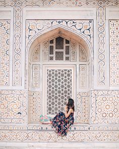 a woman sitting on a ledge in front of an ornate building with white walls and windows