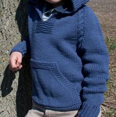 a young boy leaning against a tree wearing a blue sweater