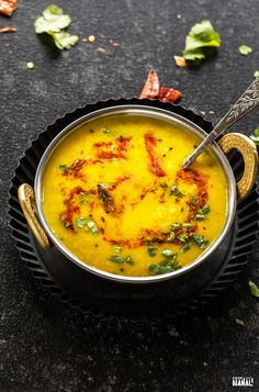 a metal bowl filled with yellow soup on top of a black table next to leaves