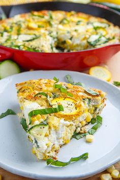 a slice of quiche on a plate with corn and green onions in the background