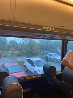 a man sitting on a bus looking out the window at cars parked in a parking lot