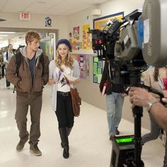 a man and woman walking down a hallway next to each other in front of a camera