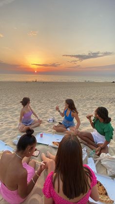 four women sitting on the beach at sunset eating pizza and watching the sun go down