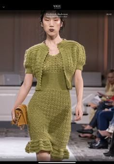 a woman is walking down the runway wearing a green dress with ruffles on it