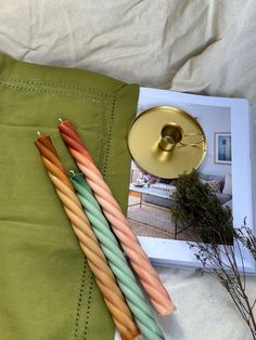 there are three different colored candles next to a book on a bed with white sheets