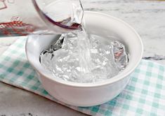 a person pouring water into a white bowl filled with ice cubes on top of a checkered table cloth